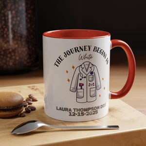 Puede incluir: Taza de cerámica blanca con interior y asa rojos. La taza presenta un gráfico de bata médica y el texto "THE JOURNEY BEGINS IN WHITE". Debajo del gráfico está el nombre "LAURA THOMPSON DDS" y la fecha "12-15-2025".