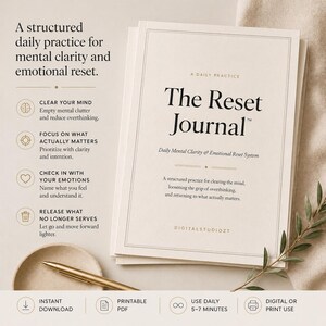 May include: A stack of cream-colored journals titled "The Reset Journal" with the text "Daily Mental Clarity & Emotional Reset System." The cover includes the text "A Daily Practice." A gold pen and decorative sprig are also visible.