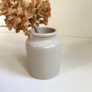 May include: A small, light gray ceramic vase with a rounded body and a slightly flared rim. The vase holds dried brown flowers, creating a natural and minimalist aesthetic. The vase is likely 4 inches tall.