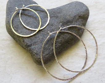 May include: Two pairs of silver hoop earrings with a hammered texture. The earrings are displayed on a gray heart-shaped rock.