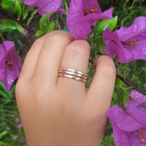 Könnte beinhalten: Drei goldene, gehämmerte Ringe, die übereinander getragen werden, an einem Finger. Die Ringe sind dünn und haben eine strukturierte Oberfläche.