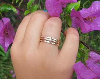 May include: Three gold hammered stacking rings on a finger. The rings are thin and have a textured surface.