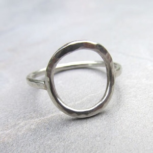 Op de afbeelding: Een zilveren ring met een gehamerd, cirkelvormig ontwerp. De ring is open en heeft een eenvoudige band.