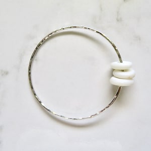 Op de afbeelding: Een zilveren gegraveerde armband met drie witte keramische ringen.