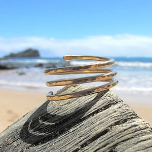 Könnte beinhalten: Ein goldfarbenes, gehämmertes Metallarmband mit einem Spiraldesign. Das Armband besteht aus vier separaten Bändern, die miteinander verdreht sind.