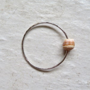 May include: A silver bangle bracelet with a single, natural seashell bead. The bead is a light brown color with white stripes.