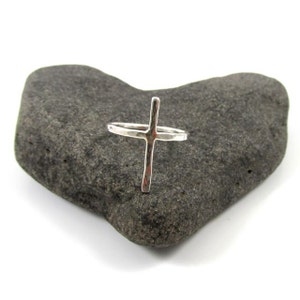 May include: A silver hammered cross ring. The ring is simple and elegant, with a minimalist design.