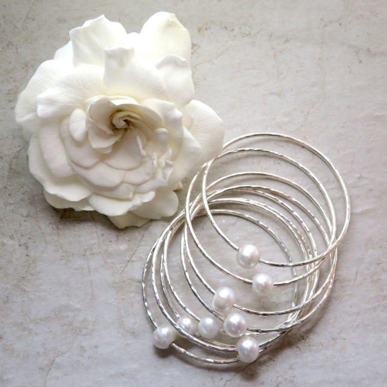 May include: A set of eight silver bangles with hammered texture and white pearl accents.