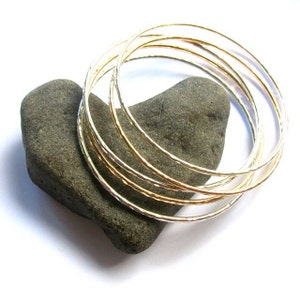 May include: A set of seven gold and silver bangles, stacked on top of each other, with a textured hammered finish.