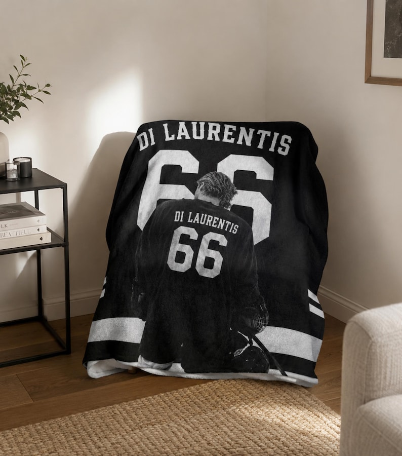 K&ouml;nnte beinhalten: Schwarz-wei&szlig;e Decke mit einem Hockey-Trikot-Design. Das Trikot zeigt den Namen "DI LAURENTIS" und die Nummer "66" in Wei&szlig;. Die Decke ist &uuml;ber einen Stuhl drapiert und zeigt das Design.