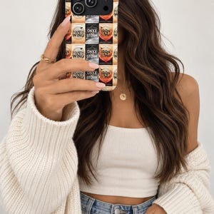 May include: A smartphone case featuring a repeating grid pattern of book covers titled Fourth Wing, Onyx Storm, and Iron Flame by Rebecca Yarros. The design includes orange, black, and red colour blocks with text and graphic elements.