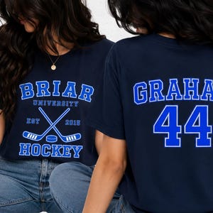 May include: A navy blue short-sleeve t-shirt featuring a front graphic with the text BRIAR UNIVERSITY HOCKEY EST 2015 and crossed hockey sticks with a puck. The back of the shirt displays the name GRAHAM in blue letters above the large blue number 44.