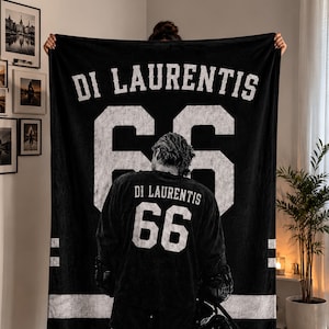 Op de afbeelding: Zwarte deken met de naam "DI LAURENTIS" en het nummer "66" in het wit. De deken heeft een hockeytrui-ontwerp met een afbeelding van een speler op de voorkant. Witte strepen bevinden zich aan de zijkanten.