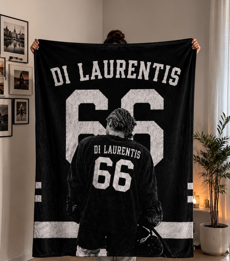 K&ouml;nnte beinhalten: Schwarze Decke mit dem Namen "DI LAURENTIS" und der Nummer "66" in Wei&szlig;. Die Decke zeigt ein Hockey-Trikot-Design mit dem Bild eines Spielers auf der Vorderseite. Wei&szlig;e Streifen befinden sich an den Seiten.