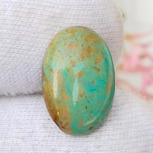 May include: An oval-shaped gemstone with a polished surface. The stone features a blend of turquoise, brown, and tan colors, creating a unique pattern. The gemstone is likely used for jewelry making or as a decorative element.