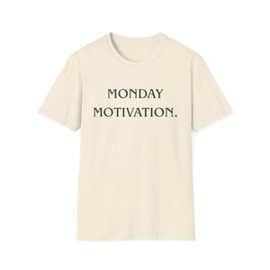 Op de afbeelding: Een crèmekleurig t-shirt met de woorden "MONDAY MOTIVATION." in het zwart gedrukt. Het shirt heeft korte mouwen en een ronde hals. De stof heeft een gespikkelde textuur.