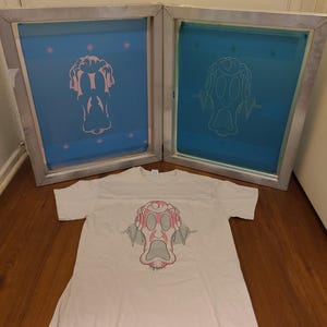 K&ouml;nnte beinhalten: Ein wei&szlig;es T-Shirt mit einer rosa-grauen Cartoon-Gesichtsgrafik. Zwei blaue Siebdruckrahmen mit dem gleichen Design befinden sich hinter dem Shirt. Das Design zeigt ein &uuml;berraschtes Gesicht mit Schallwellendetails.