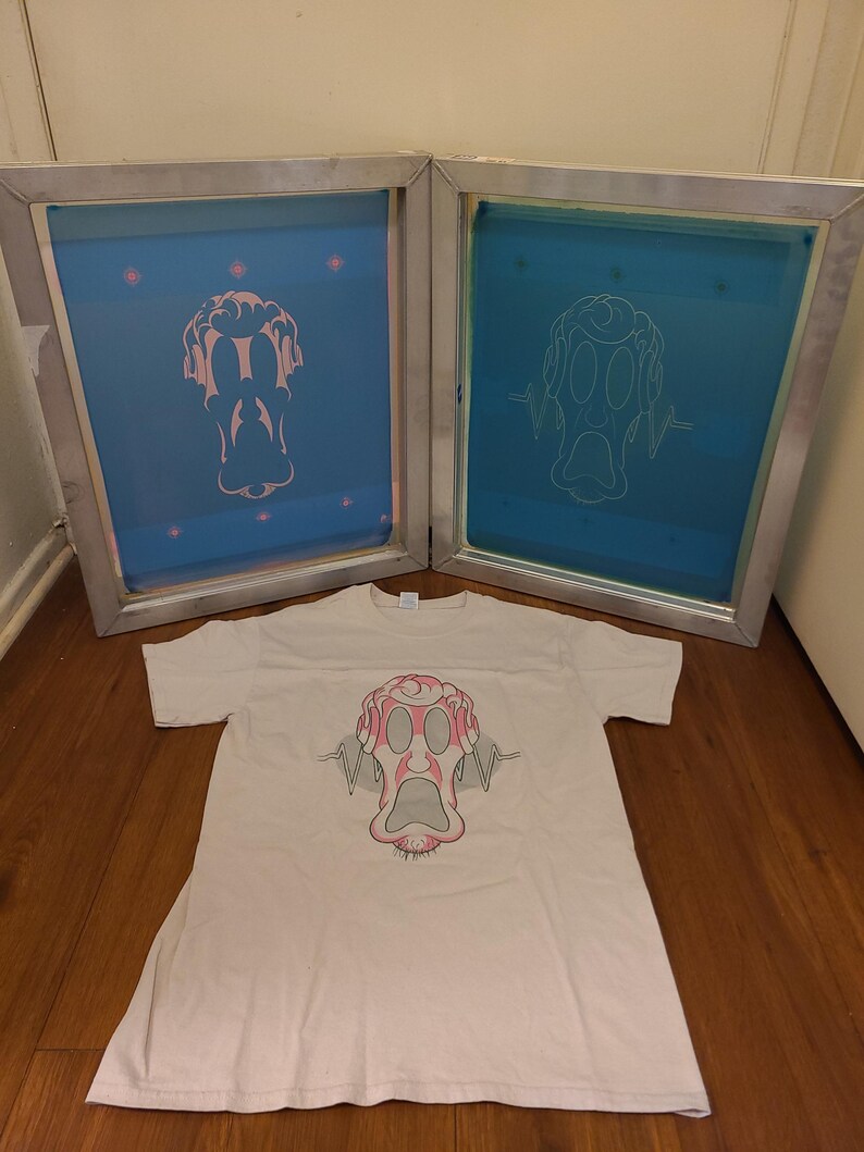 K&ouml;nnte beinhalten: Ein wei&szlig;es T-Shirt mit einer rosa-grauen Cartoon-Gesichtsgrafik. Zwei blaue Siebdruckrahmen mit dem gleichen Design befinden sich hinter dem Shirt. Das Design zeigt ein &uuml;berraschtes Gesicht mit Schallwellendetails.