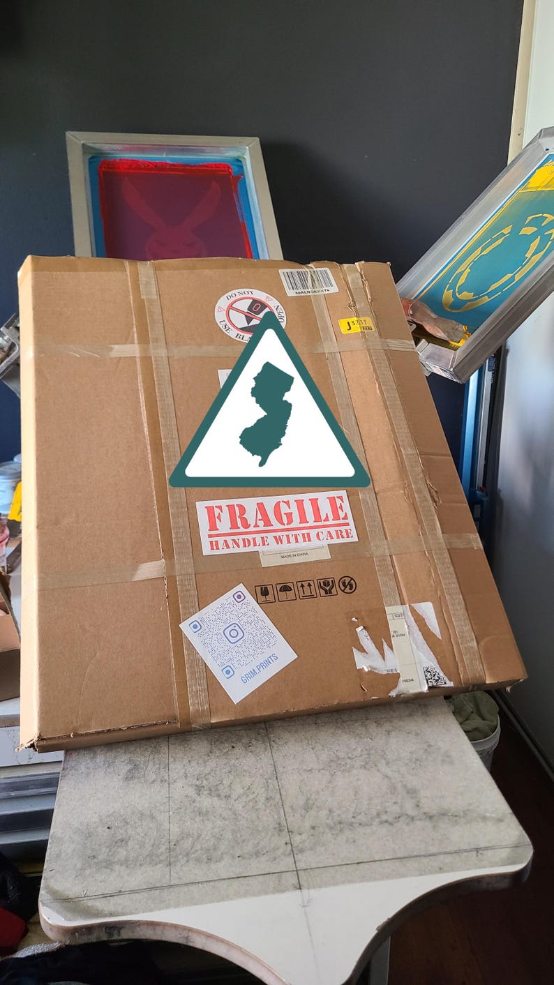 K&ouml;nnte beinhalten: Ein gro&szlig;er, versiegelter Karton mit Klebeband und einem "Zerbrechlich"-Aufkleber. Eine gr&uuml;ne und wei&szlig;e Umrisslinie des Bundesstaates New Jersey befindet sich auf der Box. Ein QR-Code und andere Versandetiketten sind ebenfalls sichtbar.
