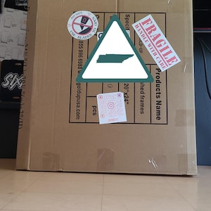 K&ouml;nnte beinhalten: Ein gro&szlig;er Karton mit verschiedenen Etiketten, darunter "FRAGILE" und "HANDLE WITH CARE." Die Box hat auch einen Aufkleber mit dem Text "DO NOT USE BLADES." Die Box enth&auml;lt "shed frames" und misst 50.8cm x 61cm.