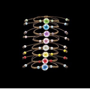 May include: A collection of handmade bracelets featuring small, colorful pressed flowers encased in clear, round settings. The bracelets have brown woven cords with adjustable closures and colorful beads.