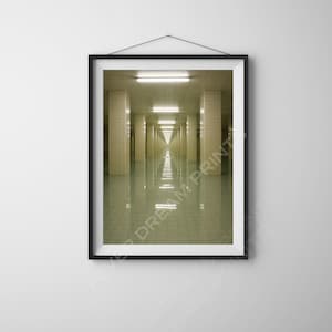 May include: A framed print of a long hallway with repeating columns and overhead lights. The floor reflects the lights and the columns, creating a symmetrical and somewhat surreal perspective. The print is in a black frame.