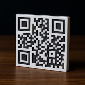 May include: A white and black QR code block, standing upright on a wooden surface. The QR code is a square with a complex pattern of black and white squares and rectangles. The edges of the block are white.