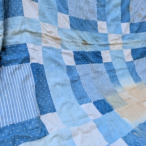 May include: A patchwork quilt featuring a variety of blue and white fabric squares. The design incorporates light blue, dark blue, and white patterns including stripes, polka dots, and solid colors, joined with visible white hand-tied knots.