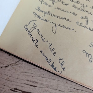 May include: A piece of aged, light tan paper featuring dark ink handwritten cursive text. The visible script includes phrases such as 'Sophmore class this year' and 'Yours till the concrete walks'. The paper has a visible texture and vintage appearance.