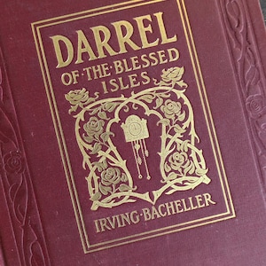 May include: A hardcover book with a deep burgundy cover featuring gold foil stamping. The front cover displays the title DARREL OF THE BLESSED ISLES and the author IRVING BACHELLER, surrounded by a decorative frame of roses and a clock icon.