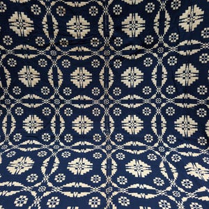 May include: A woven textile featuring a repeating geometric pattern in dark navy blue and off-white. The design consists of interconnected star-like shapes and small square motifs arranged in a grid, with a visible vertical seam running down the center.
