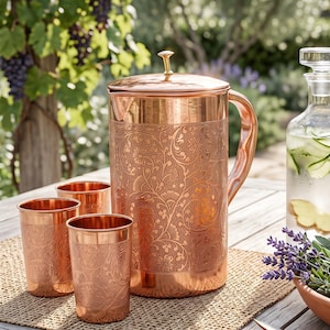 May include: A copper pitcher with a matching set of three copper tumblers, all featuring an intricate embossed floral pattern. The pitcher includes a lid with a small knob handle and a curved side handle, while the tumblers are cylindrical.