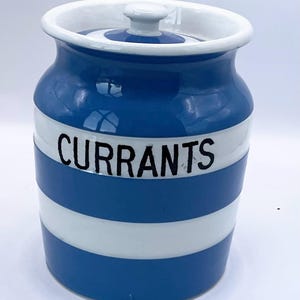 May include: A ceramic jar with a lid, painted in blue and white horizontal stripes. The word "CURRANTS" is printed in black across the center. The jar has a white rim and a small knob on the lid.