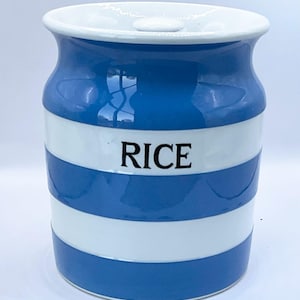 Può includere: Un contenitore per riso in ceramica con coperchio bianco e motivo a righe blu e bianche. La parola "RICE" è stampata in nero sul davanti. Il contenitore ha una forma cilindrica.