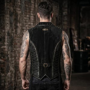 May include: Black vest with a studded collar and decorative metal accents. The vest features a lace-up back and a buckle closure. The vest is made of a dark material and has a tailored fit.