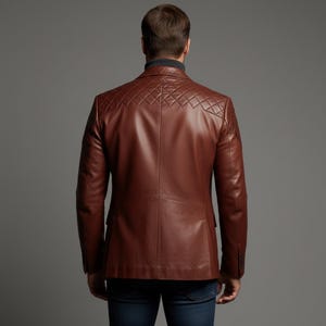 May include: A brown leather blazer with diamond-stitched shoulder accents. The jacket has a classic two-button closure and a notched lapel. The model is wearing a dark turtleneck and blue jeans.