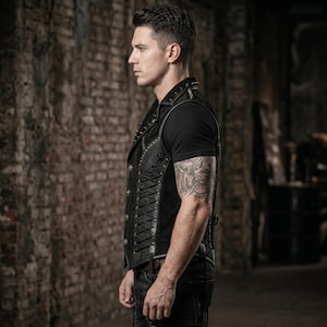 May include: Black leather vest with decorative metal studs and floral embossed panels. The vest features a lace-up side detail and is worn over a black t-shirt. The vest is a stylish piece of apparel.