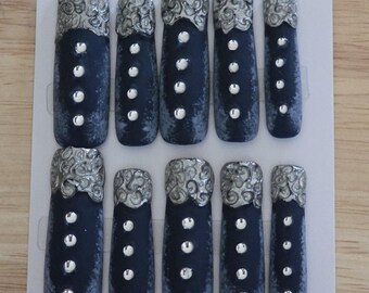 May include: Set of ten navy blue press-on nails with silver decorative tops and silver button-like accents. The nails are arranged on a white card, showcasing a unique and elegant design.