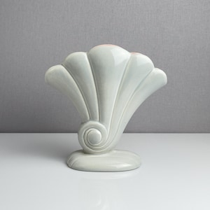 May include: A light green ceramic vase in a fan shape with a swirl design at the base. The vase has a wide, rounded base and a series of curved, fluted sections that form the fan shape. The vase is approximately 10 inches tall.