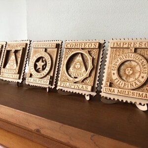 May include: Five rectangular wooden plaques shaped like postage stamps, each featuring intricate laser-cut designs. The plaques display historical text including 'RECIBOS', 'TELEGRAFOS', 'CERTIFICADO', 'CORREOS', and 'IMPRESOS' alongside symbols like stars and suns.