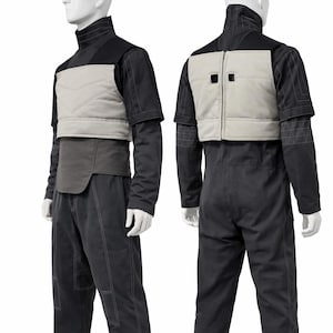 Op de afbeelding: Een tweedelig kostuum op een mannequin. De outfit bevat een zwart shirt met lange mouwen en een hoge kraag, een lichtgrijs vest en een zwarte broek. Het vest heeft een rits en twee vierkante details. Witte stiksels accentueren de broek.