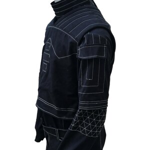 Puede incluir: Chaqueta negra con costuras blancas. La chaqueta presenta un cuello alto, hombreras y patrones geom&eacute;tricos en las mangas. Tiene bolsillos y un cintur&oacute;n. Las costuras blancas crean un dise&ntilde;o contrastante.