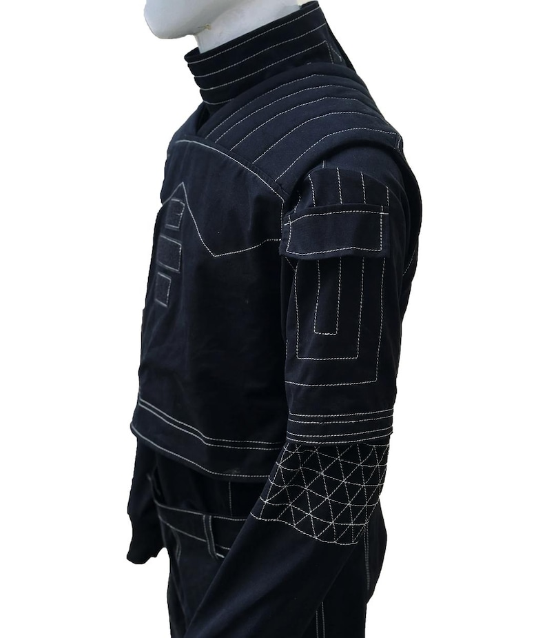 Puede incluir: Chaqueta negra con costuras blancas. La chaqueta presenta un cuello alto, hombreras y patrones geom&eacute;tricos en las mangas. Tiene bolsillos y un cintur&oacute;n. Las costuras blancas crean un dise&ntilde;o contrastante.