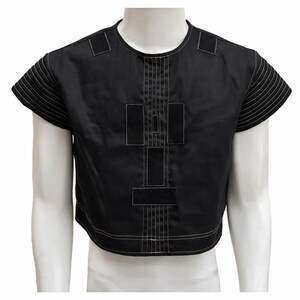 May include: Black crop top with white stitching details. The top features a crew neck, short sleeves with horizontal stitching, and a geometric design on the front. The garment is displayed on a white mannequin.