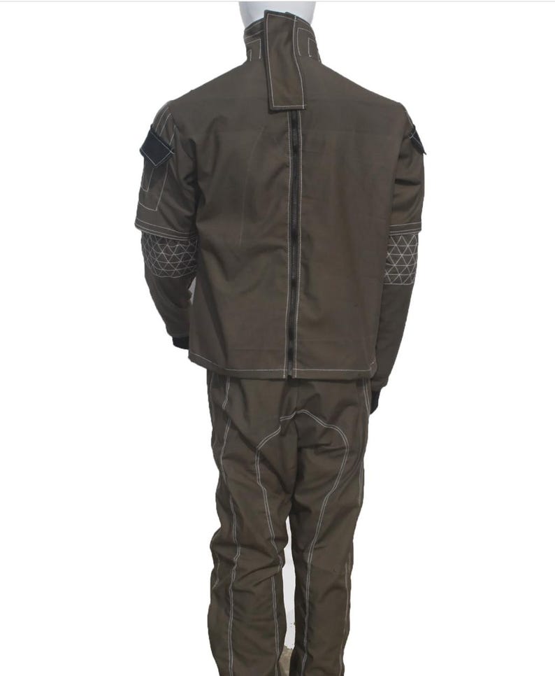 May include: A brown two-piece suit with white stitching. The jacket has a high collar and a zipper down the back. The sleeves have geometric patterns. The pants have white stitching down the front.