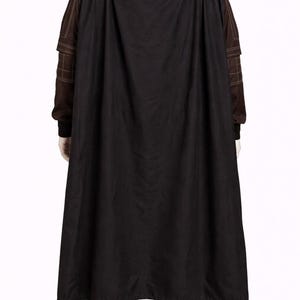 Puede incluir: Una capa negra sobre un atuendo marr&oacute;n. El atuendo incluye una camisa de manga larga y pantalones. La tela marr&oacute;n tiene costuras visibles. La capa es larga y llega hasta los tobillos. El atuendo parece ser un disfraz.