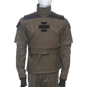 May include: Olive green jumpsuit with a high collar and black accents. The suit features white stitching details, a chest patch, and black cuffs. The sleeves have a layered design. The outfit is displayed on a mannequin.