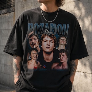 May include: A black short-sleeve t-shirt featuring a graphic print with the text ROZANOV and Ilya. The design includes multiple photographic portraits of the same person in various poses, with some images showing a cigarette and a necklace.