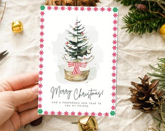 May include: A Christmas greeting card with a watercolor illustration of a Christmas tree in a basket, adorned with a red and white striped bow. The card is framed with a pink snowflake border and includes the text "Merry Christmas!" and a holiday message.