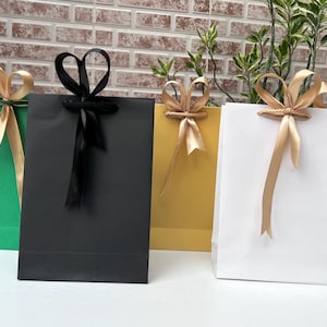 Peut inclure: Plusieurs sacs cadeaux colorés en vert, noir, jaune, blanc et orange. Chaque sac est orné d'un nœud en ruban assorti. Les sacs sont disposés en rangée, parfaits pour offrir des cadeaux.